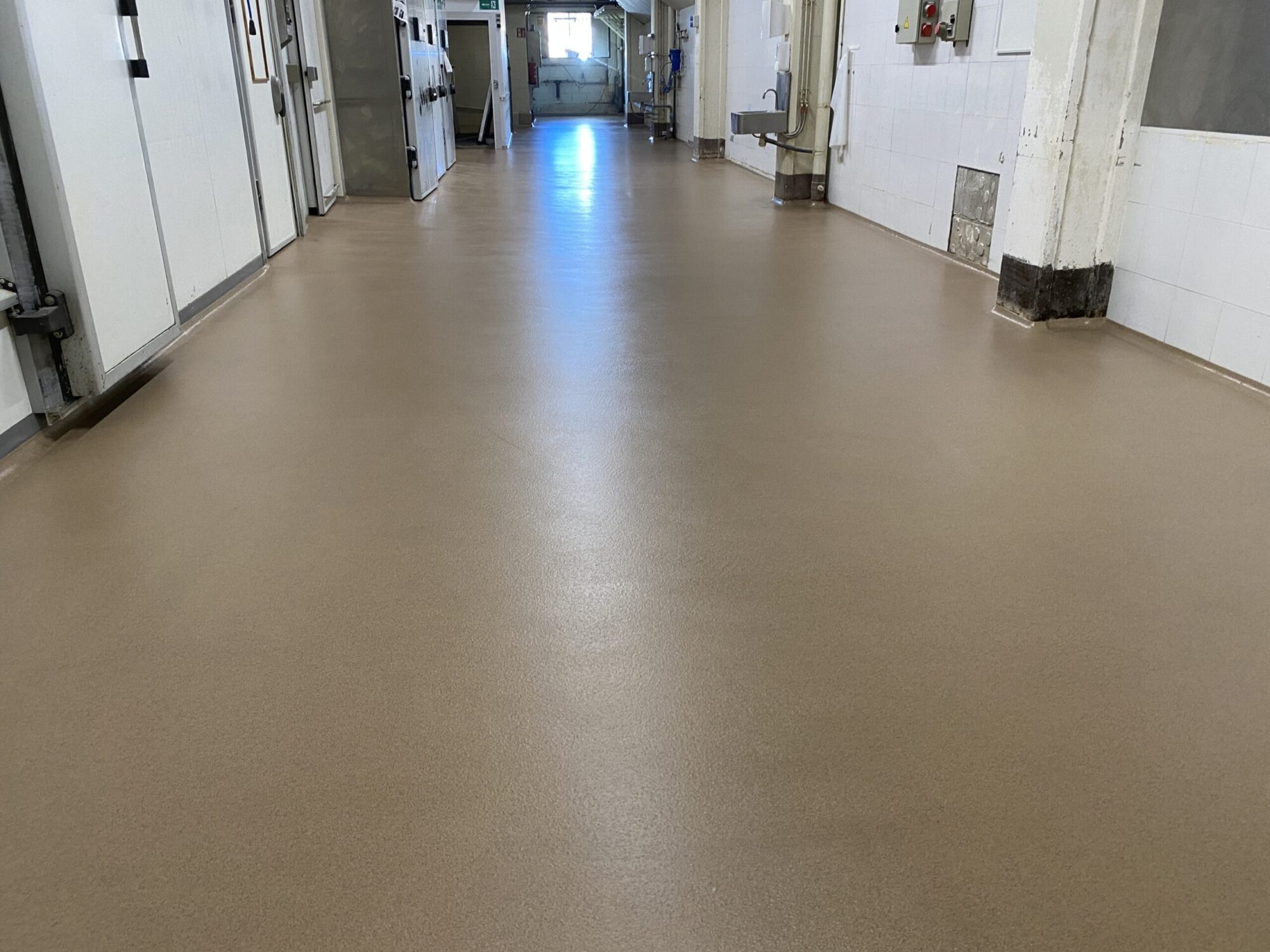 Pavimento multicapa de resina de metacrilato en color marrón beige aplicado en un pasillo.
