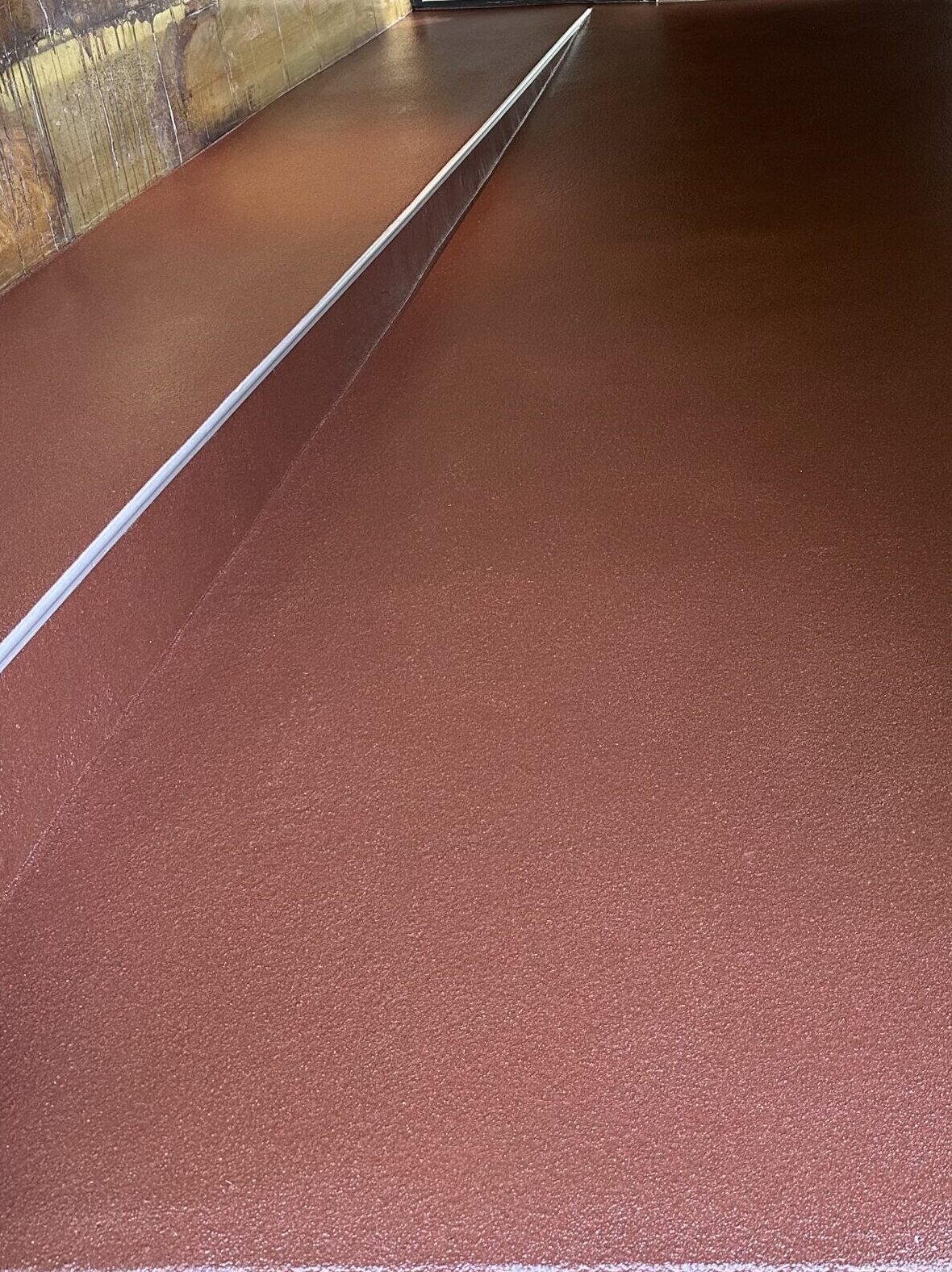 Rampa recubierta de resina de metacrilato color rojiza y con un perfil instalado.