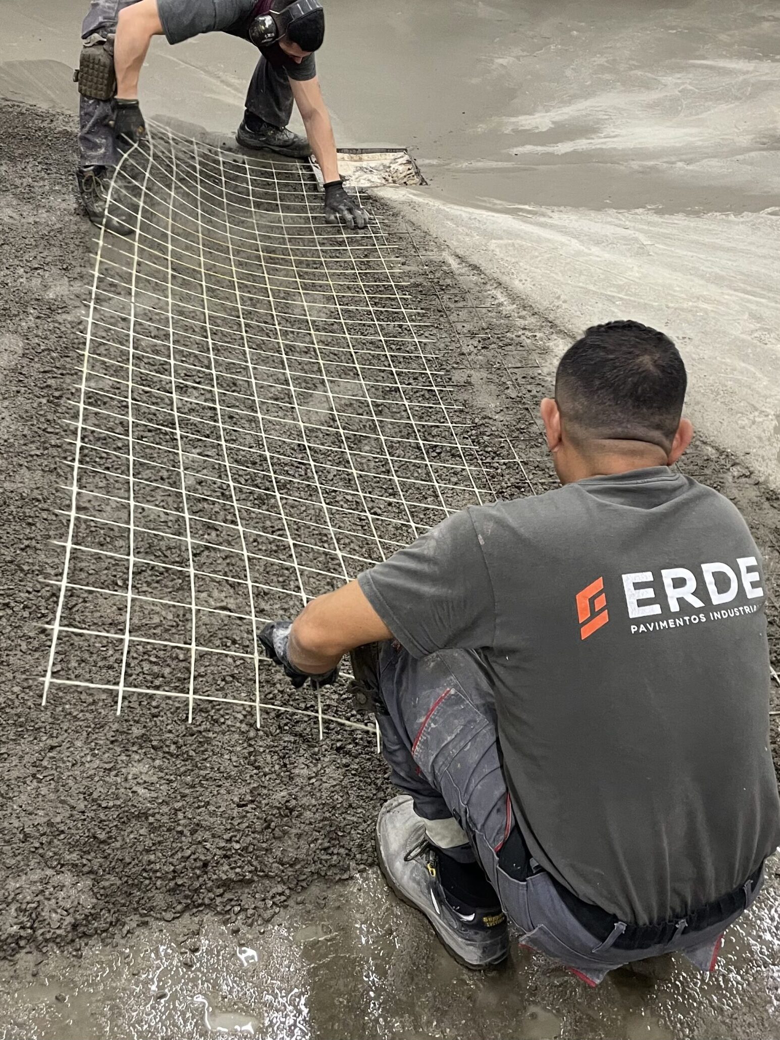 Dos operarios de Erde Pavimentos aplicando un mallazo sobre pavimento.